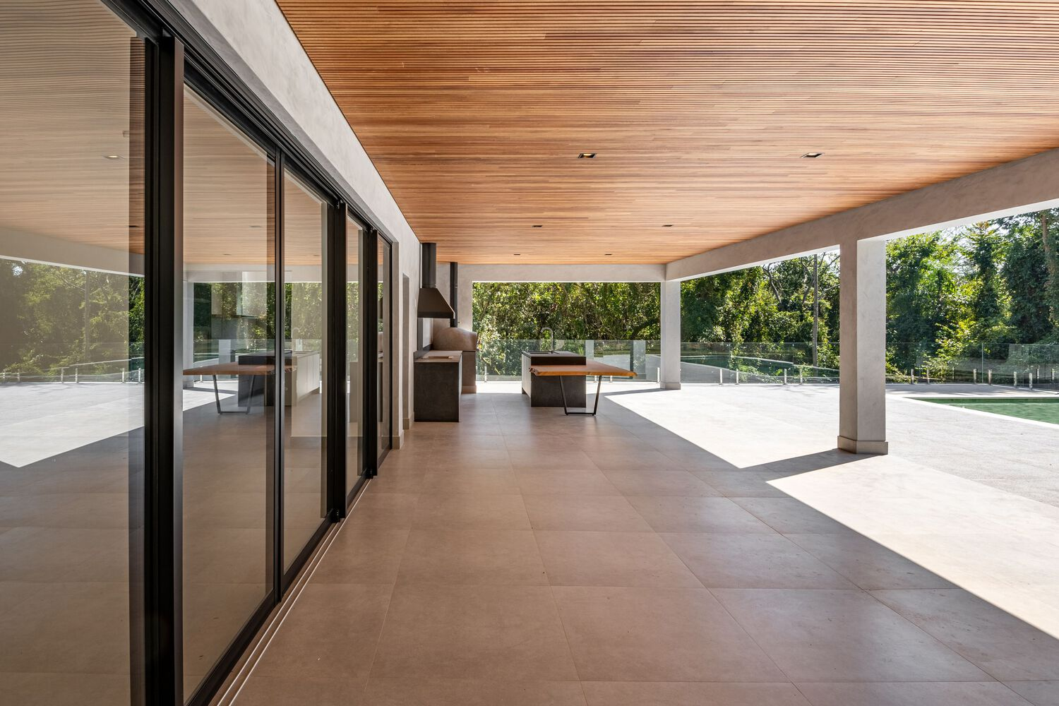 Covered terrace with wood ceiling, sliding glass doors and outdoor kitchen opening to lawn