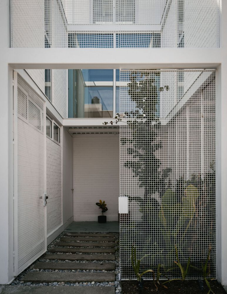 Courtyard entry with concrete stepping stones on gravel leading to a perforated metal screen wall