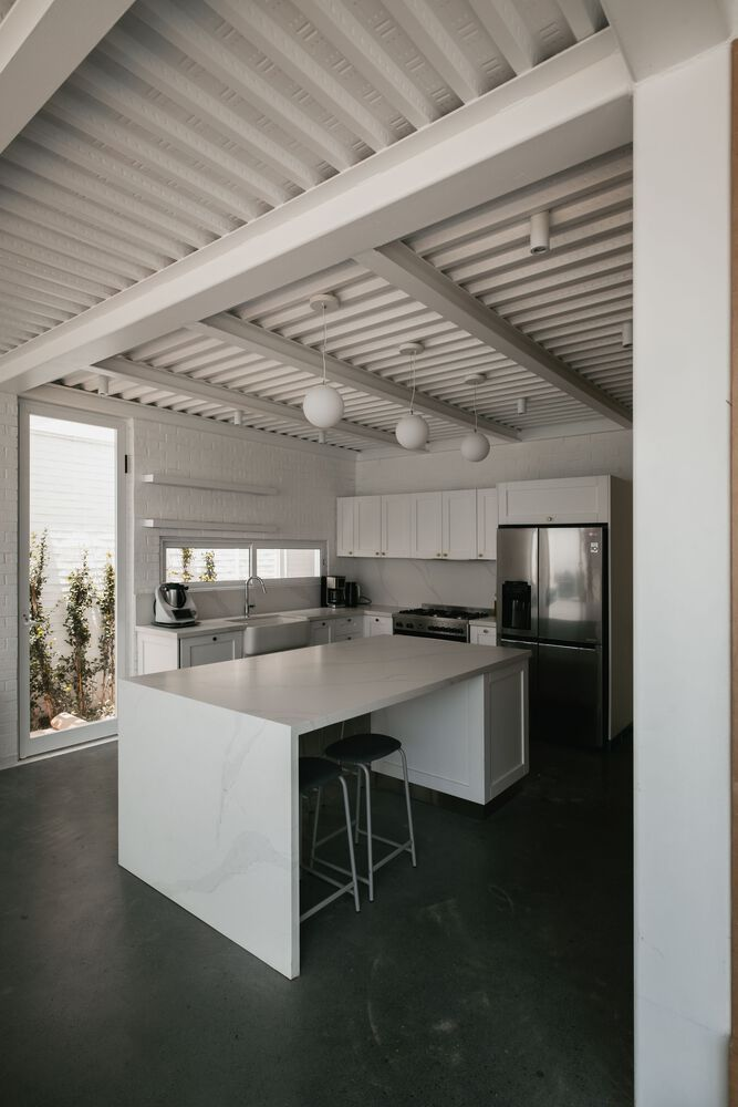 Kitchen with white island and slatted ceiling beams casting shadows across polished concrete floor