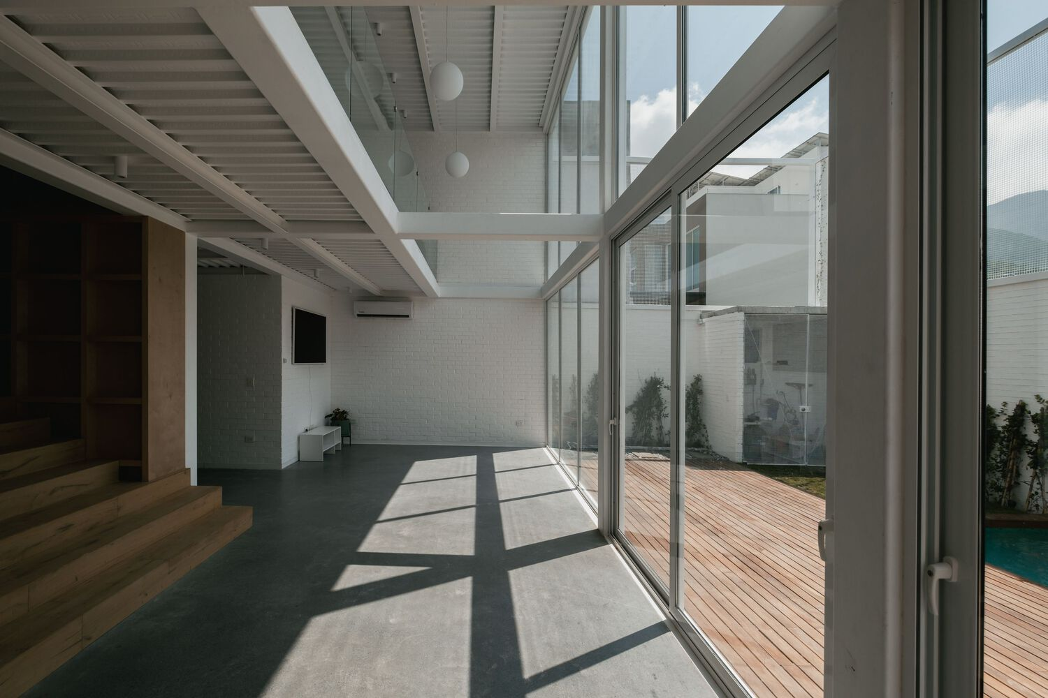 Glass wall opening to timber deck with sunlight casting diagonal shadows on concrete floor