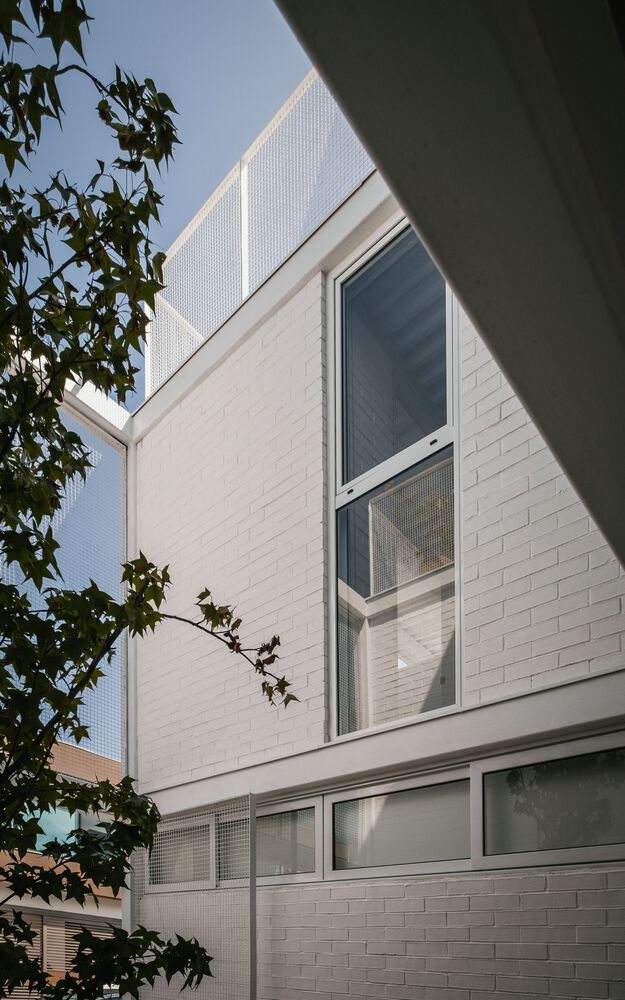 White brick facade with perforated metal screen tower framed by tree branches against clear sky