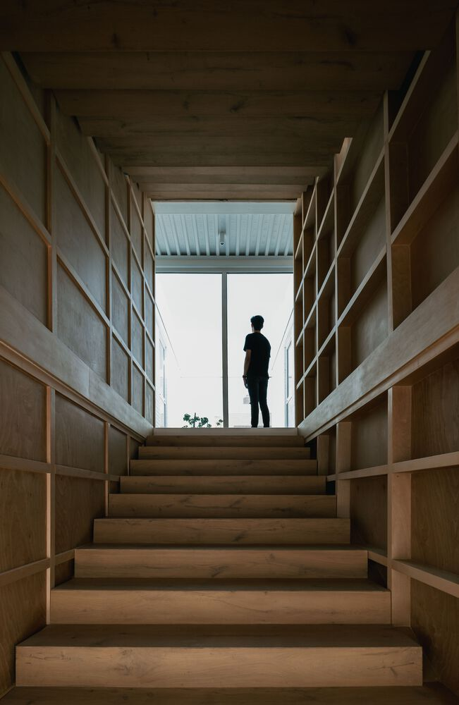 Timber staircase flanked by built-in shelving with silhouette of person standing at skylit landing