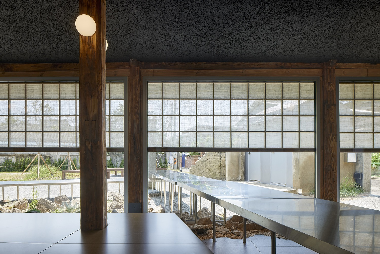 Interior view through timber-framed shoji screens with elevated steel table bridging exposed earth beneath