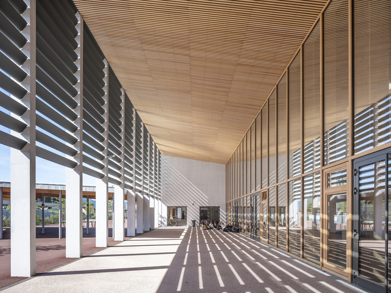 Covered corridor with horizontal timber louvres casting striped shadows across the floor in bright sun