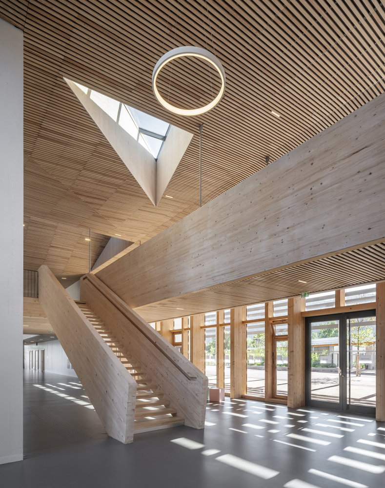 Timber staircase rising beneath triangular skylight and circular pendant light in double-height foyer