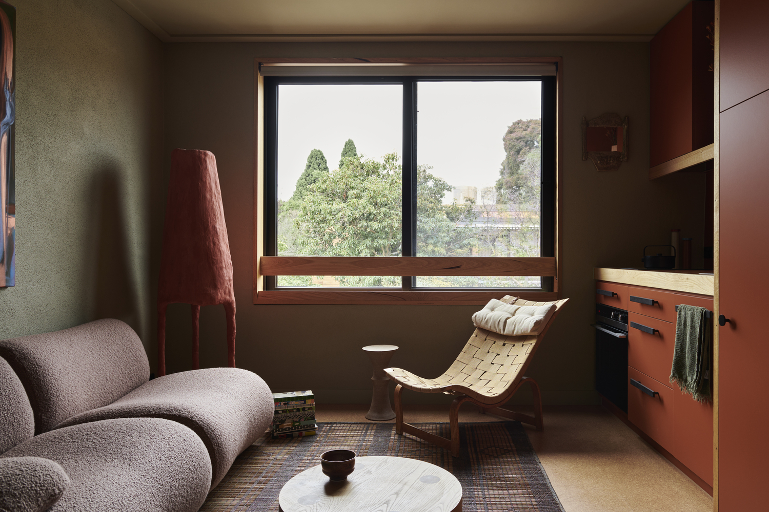 Living room with timber-framed window overlooking green treetops in soft daylight