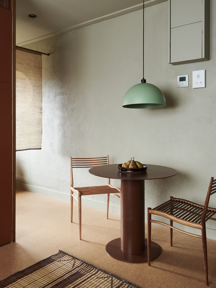 Dining area with cylindrical brown table beneath a green pendant lamp