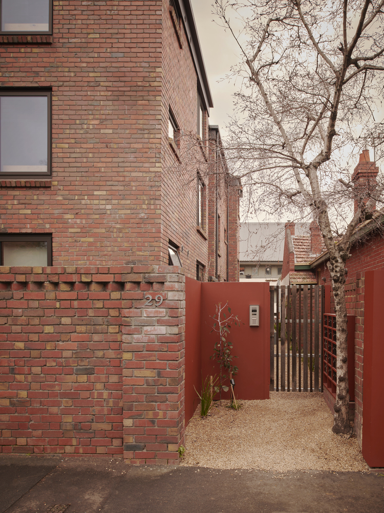 Brick entry courtyard with red metal gate and bare winter tree