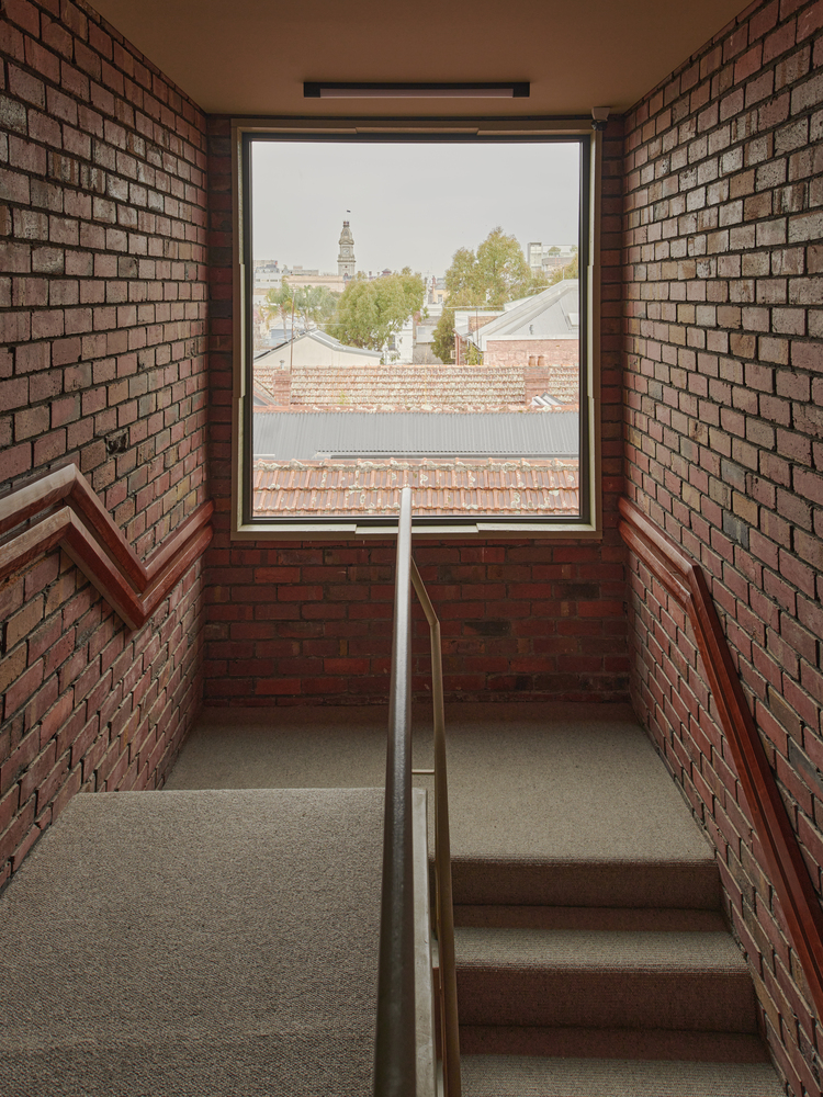 Stairwell landing with exposed brick walls framing a window onto rooftops
