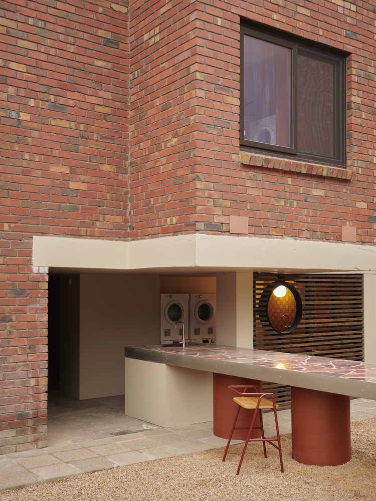Ground-floor communal laundry niche with white bench counter and red cylindrical base beneath variegated brick wall