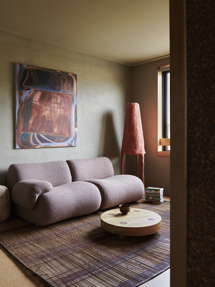 Living room with textured sofa and conical lamp in afternoon sunlight filtered through a narrow window