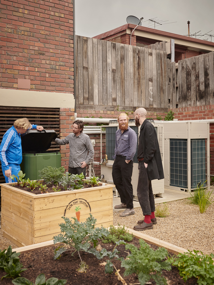 Rear courtyard with timber planter boxes and four residents gathered near the brick and weathered timber facade