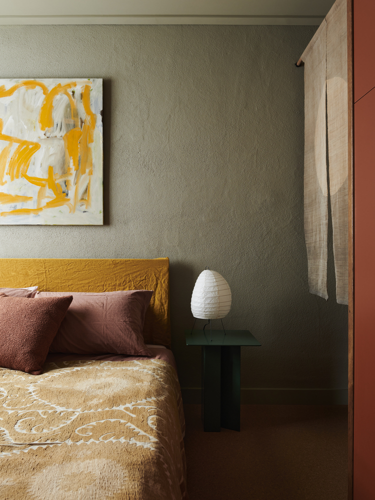 Bedroom corner with sage green walls, timber sliding door jamb and dark glass bedside table with white lamp