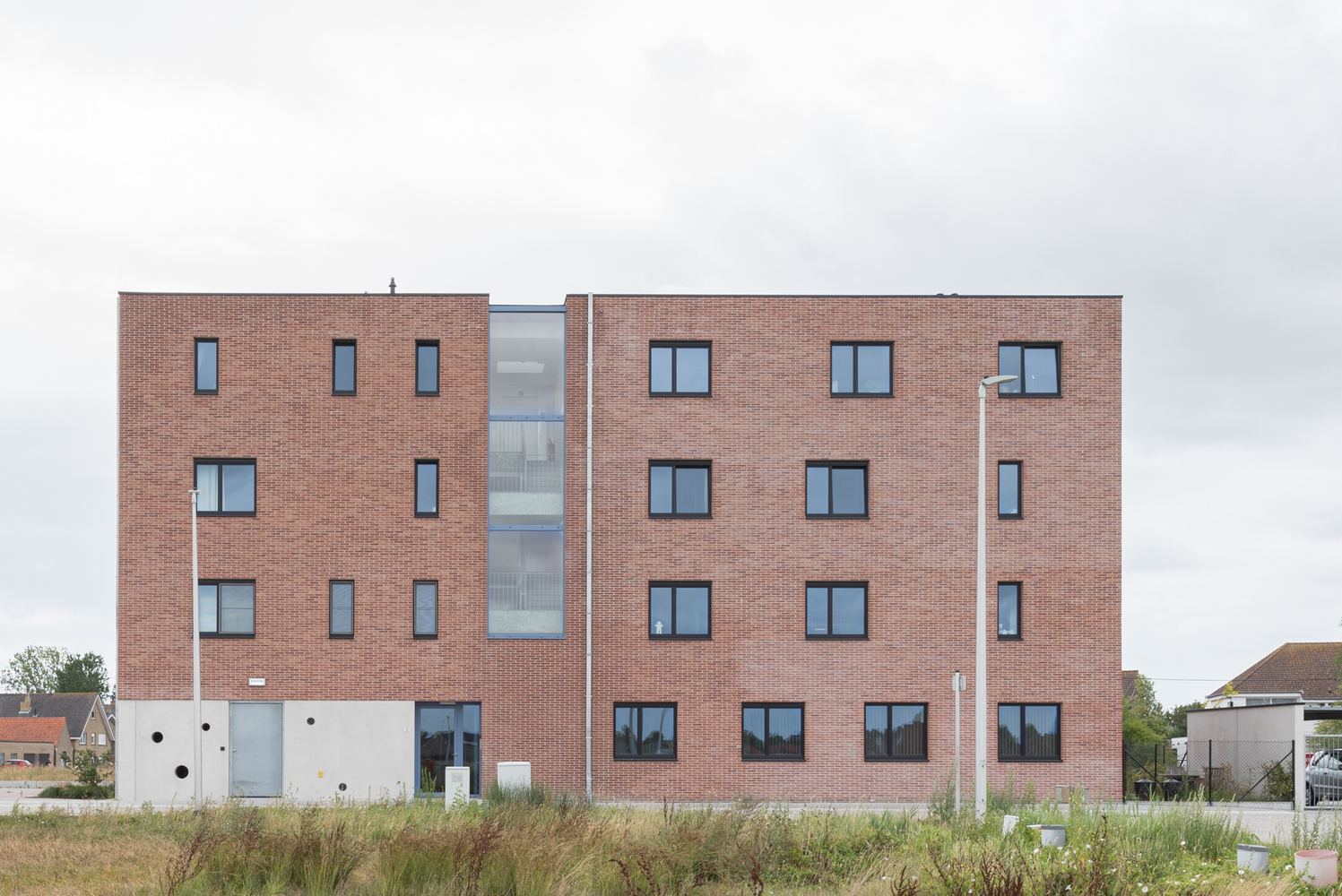 Rear elevation showing red brick volumes flanking a central glazed circulation core under overcast sky