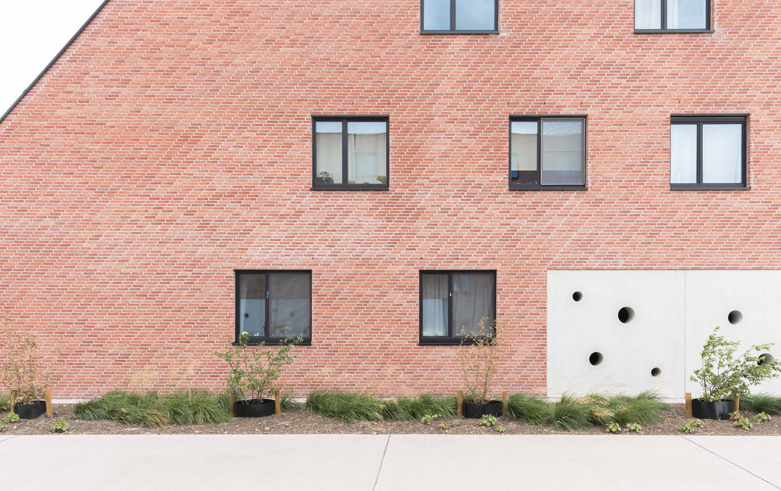 Red brick facade with rectangular windows and white panel punctured by circular openings at ground level