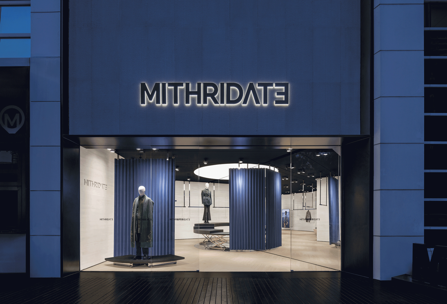 Storefront entrance with illuminated signage and blue composite panel facade at dusk