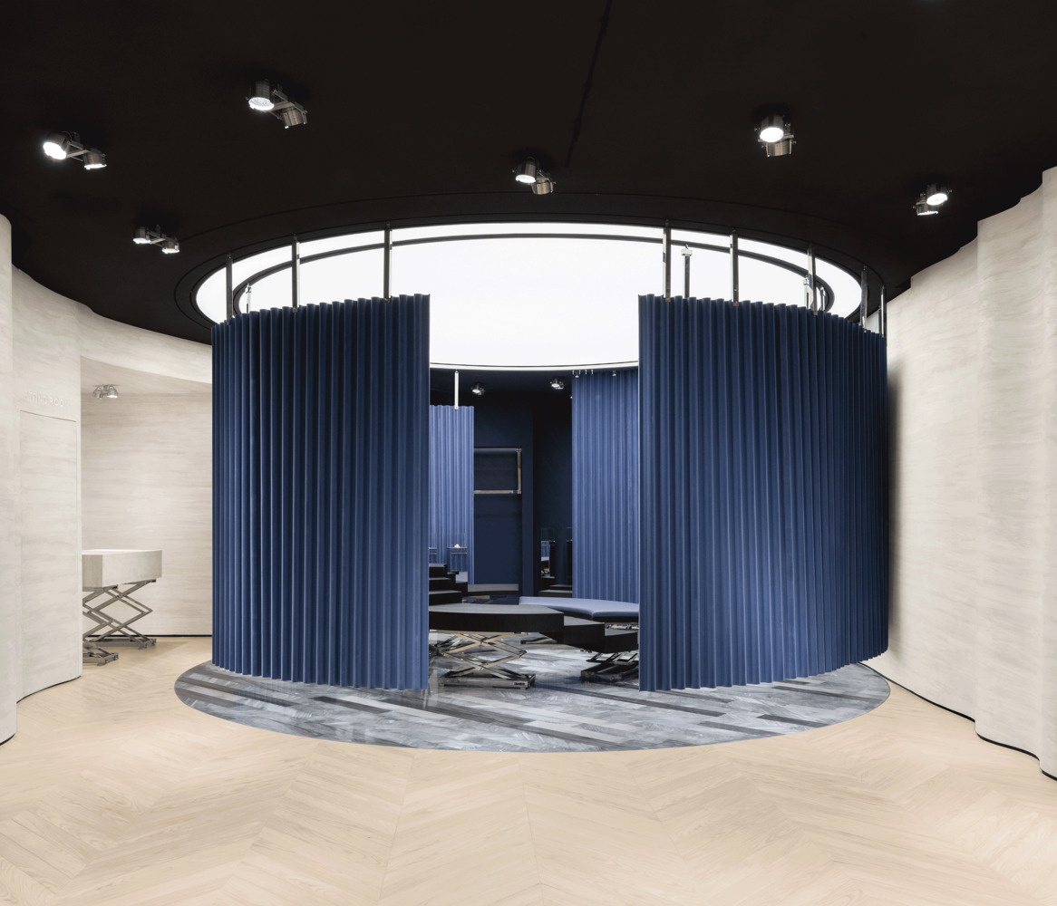 Circular fitting area enclosed by blue pleated curtains beneath a white ring skylight
