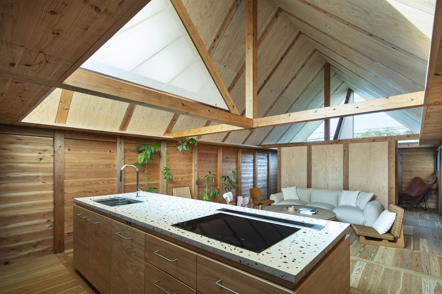 Open kitchen with terrazzo island beneath a vaulted timber ceiling with exposed beams and triangular skylights