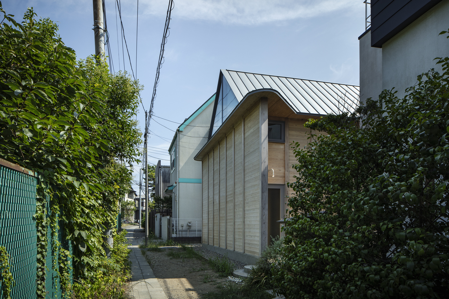 Street view of the timber-clad facade with curved gable and standing seam metal roof between neighboring buildings