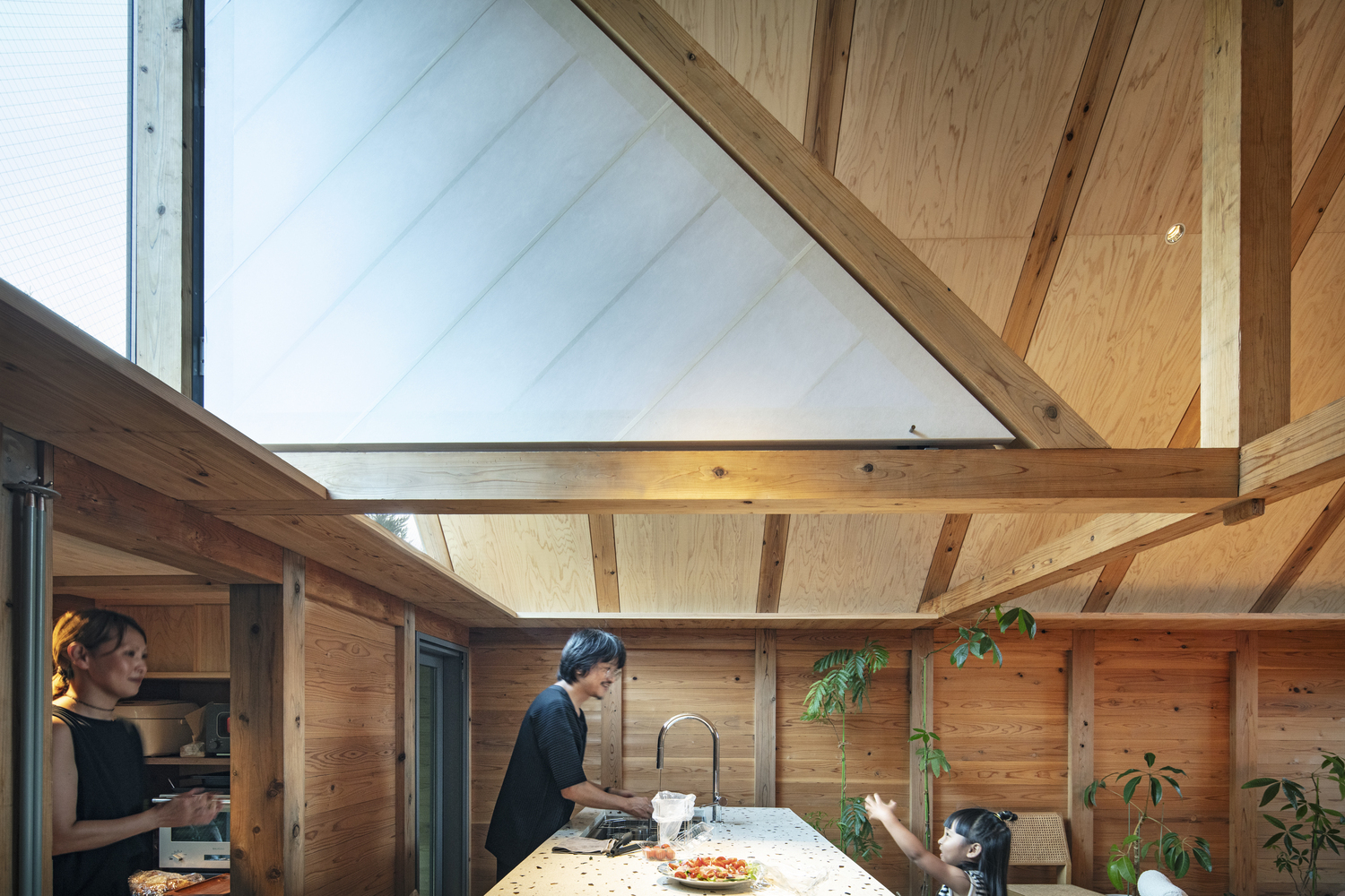 Kitchen island with two occupants preparing food under vaulted timber ceiling with clerestory glazing above