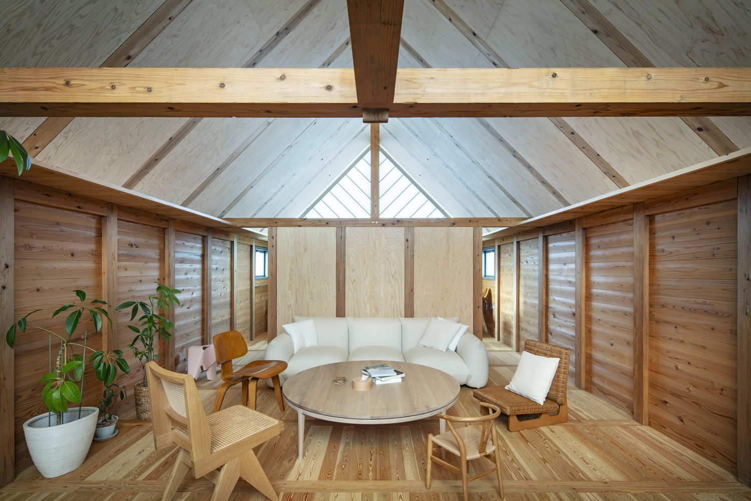 Living space with curved sofa and round table under vaulted timber ceiling with central skylight