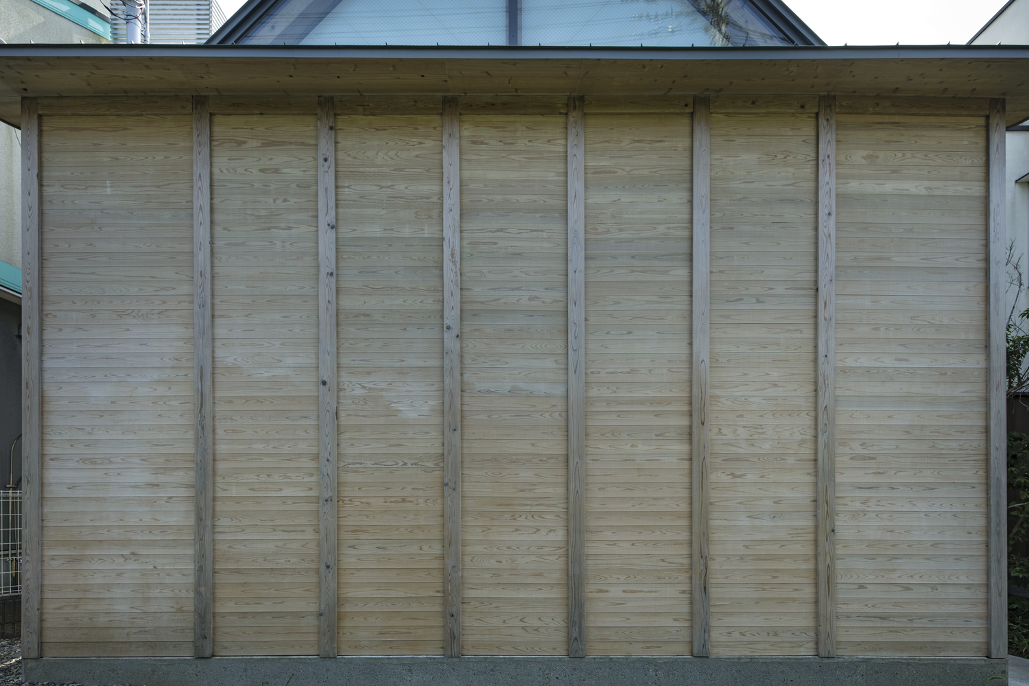 Exterior wall of horizontal bamboo siding between vertical timber structural columns beneath a sheltering roof