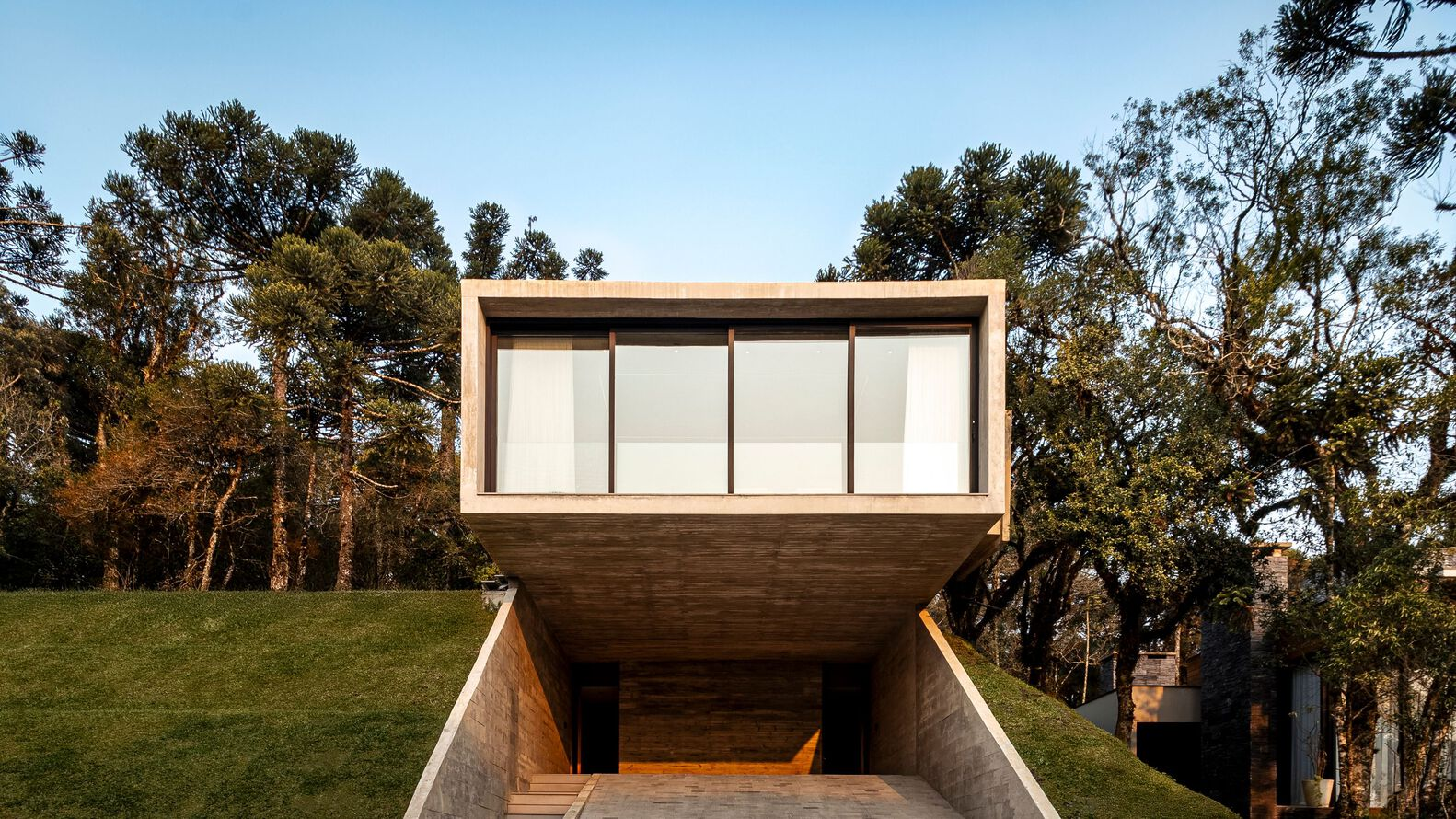 Timber-clad box suspended over concrete ramp entry framed by afternoon light