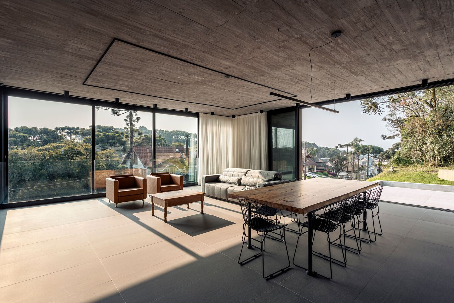 Open living pavilion with board-formed concrete ceiling and floor-to-ceiling glass overlooking hillside