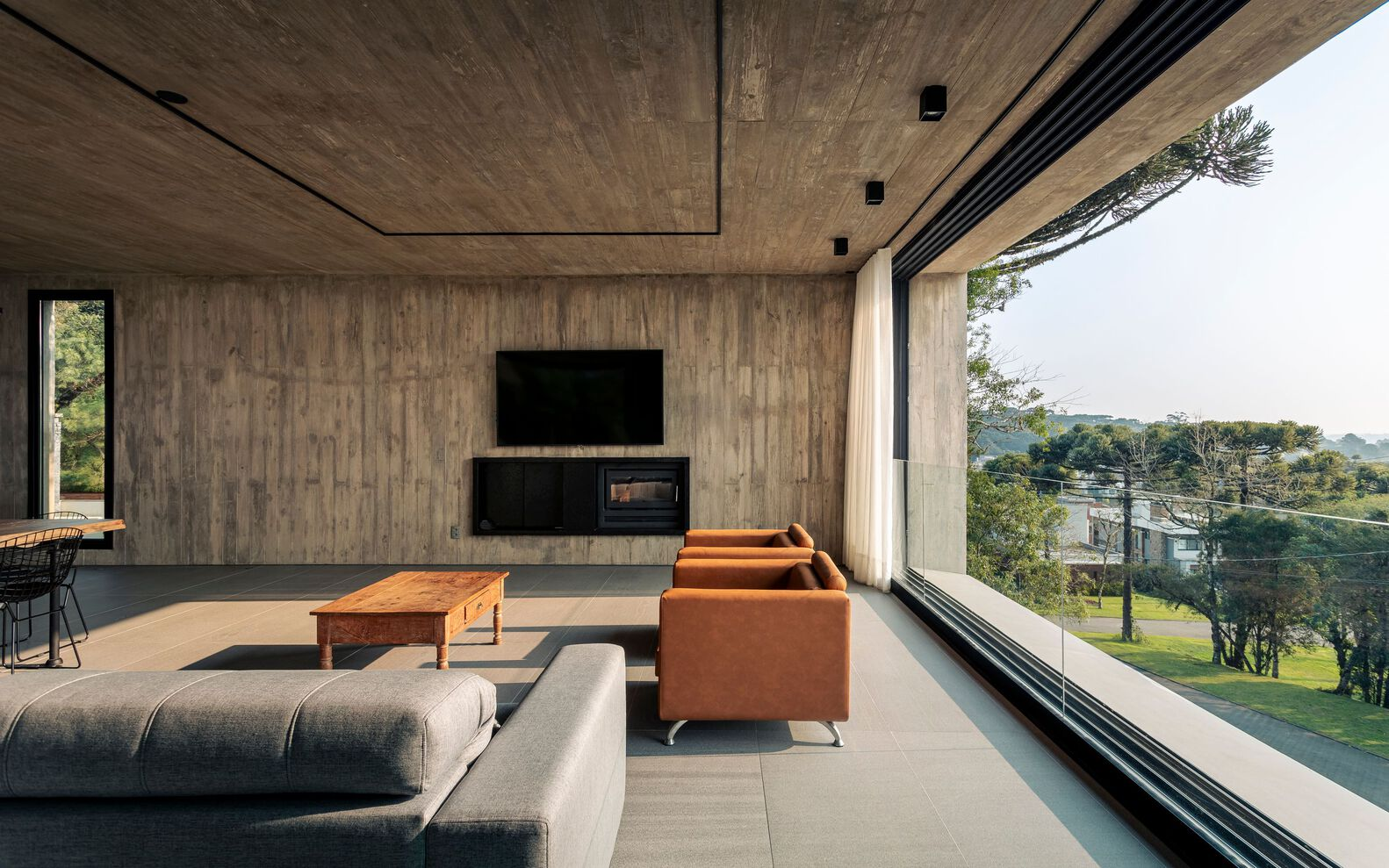 Living room with board-formed concrete ceiling and full-height glazing overlooking treetops