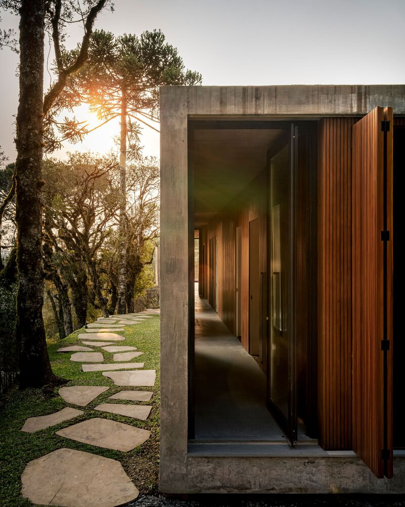 Timber-lined entry corridor framed by concrete walls and pivoting slat door at sunset