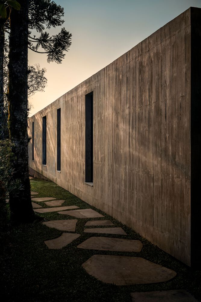 Board-formed concrete wall with vertical windows beside stepping-stone path at dusk
