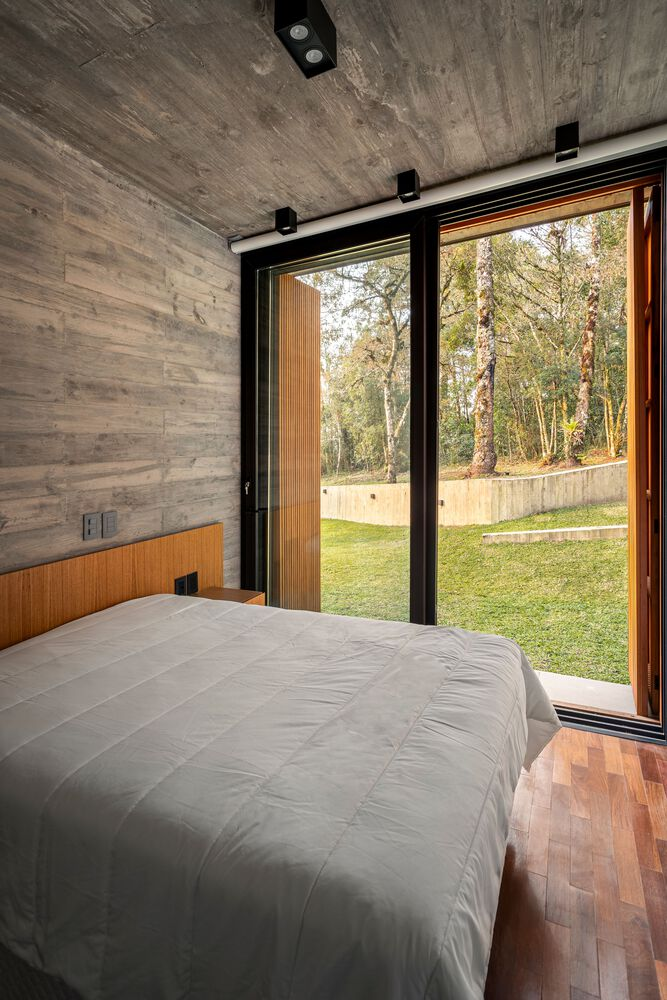 Bedroom with board-formed concrete walls and ceiling opening to a lawn through sliding glass doors