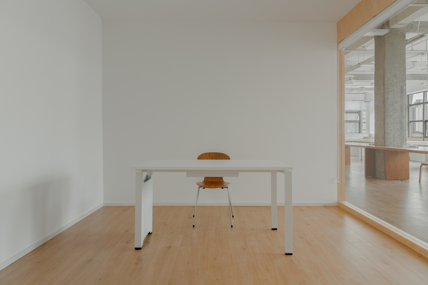 Single white work table with orange chair in a minimal room framed by plywood trim