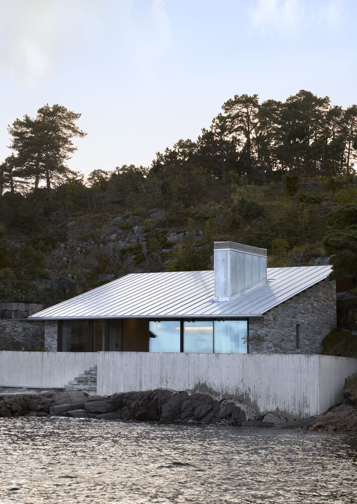 Lakeside elevation at dusk showing the metal roof and central chimney mass against the rocky hillside
