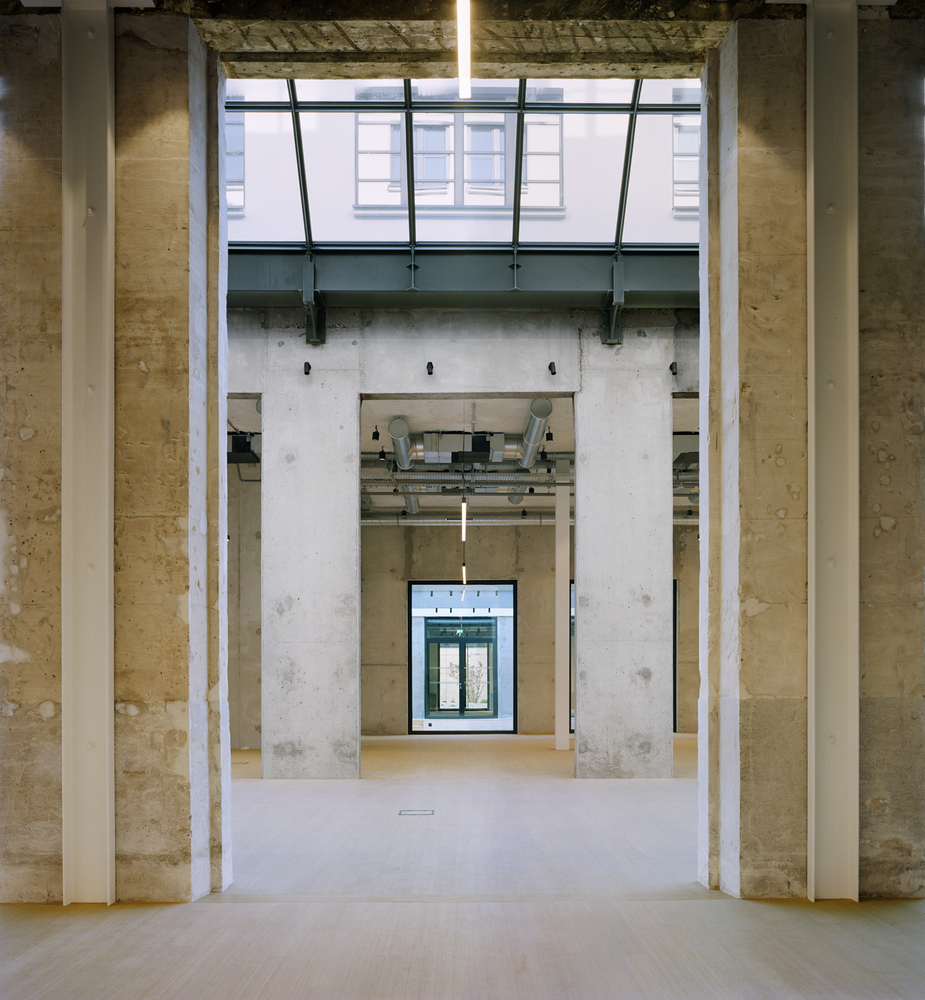 Axial view through concrete columns and doorways with exposed ceiling ducts and clerestory glazing