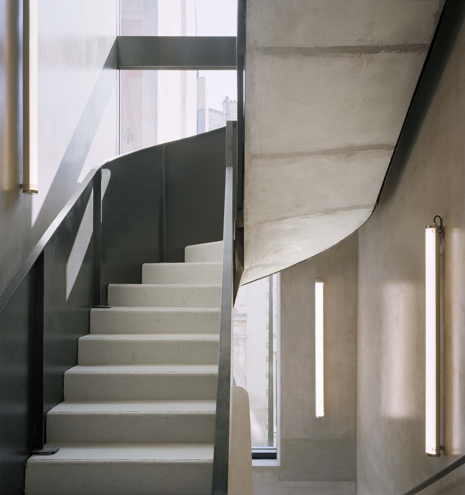 Precast concrete staircase curving upward with dark metal balustrade and vertical strip lighting