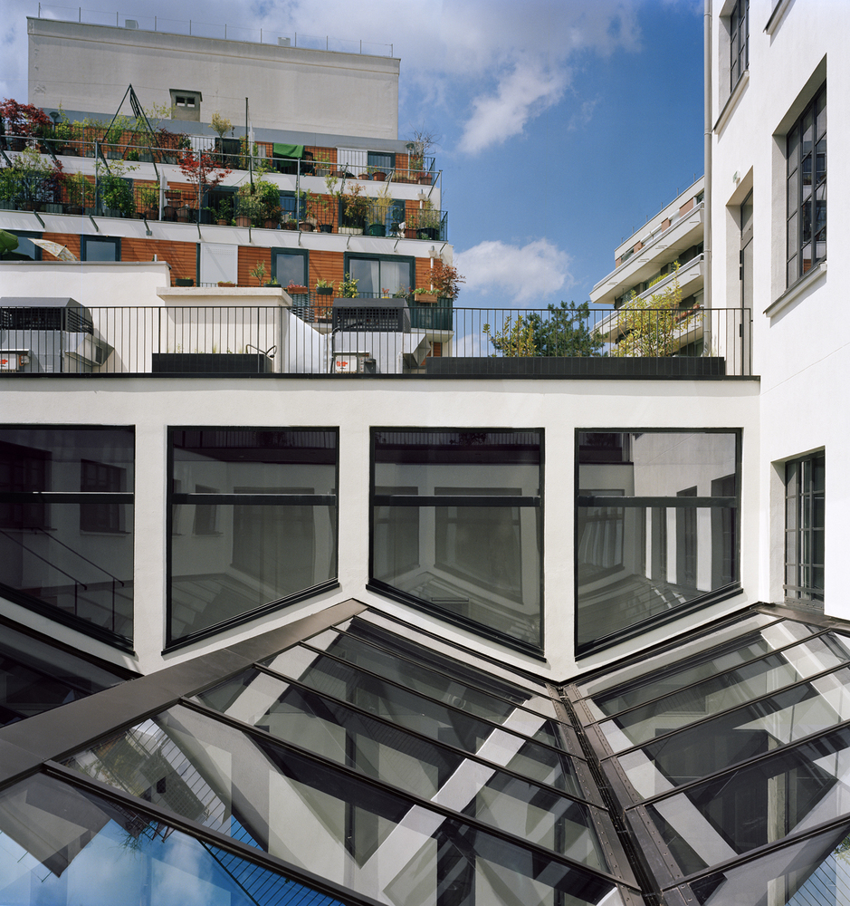 Courtyard view showing projecting white-framed windows above angled glass skylights with planted terrace beyond