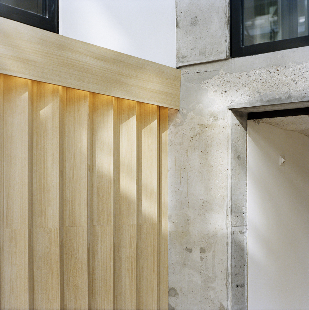 Detail of vertical timber paneling meeting raw concrete column with light washing across the surfaces