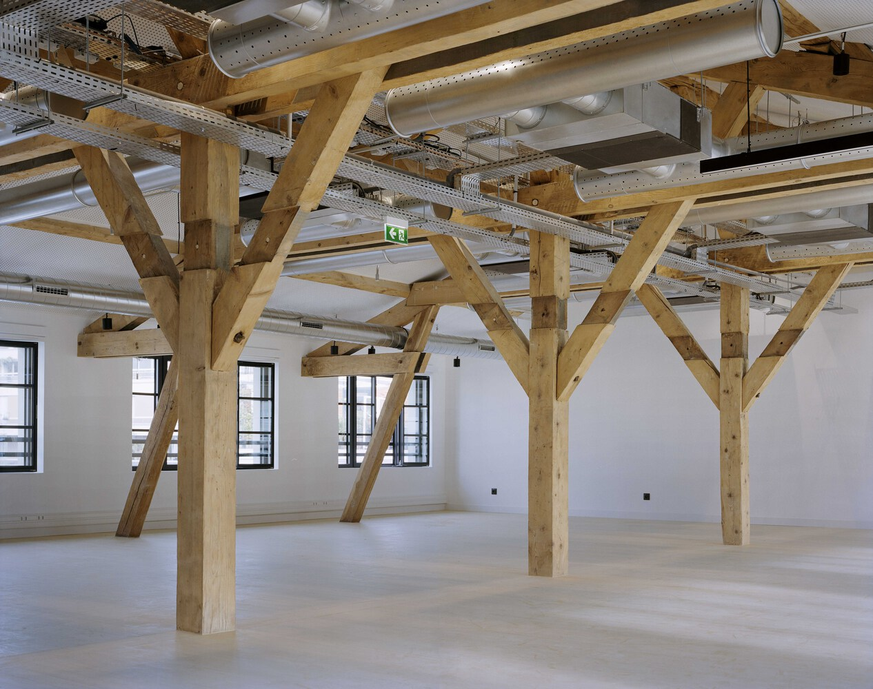 Interior space showing diagonal timber trusses with exposed mechanical ducts and linear lighting above pale floors