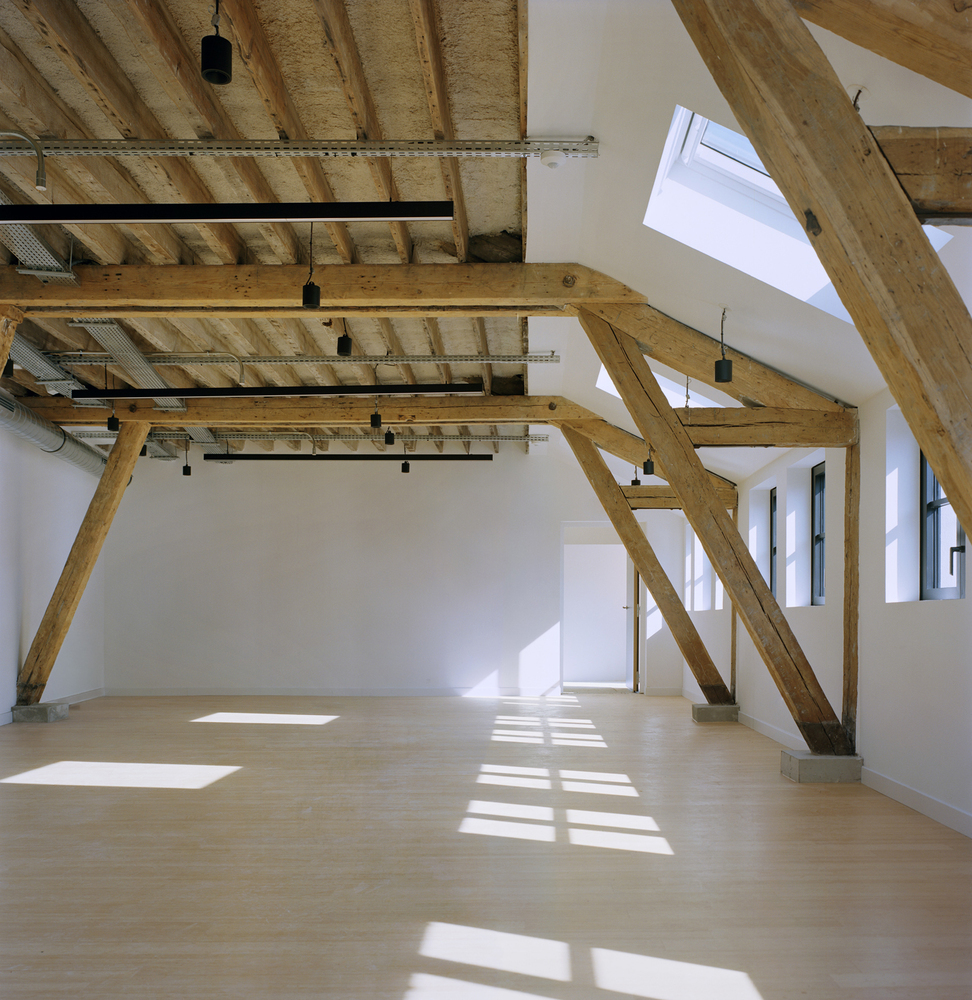Upper floor interior with exposed timber trusses and joists, white walls, and sunlight through skylights