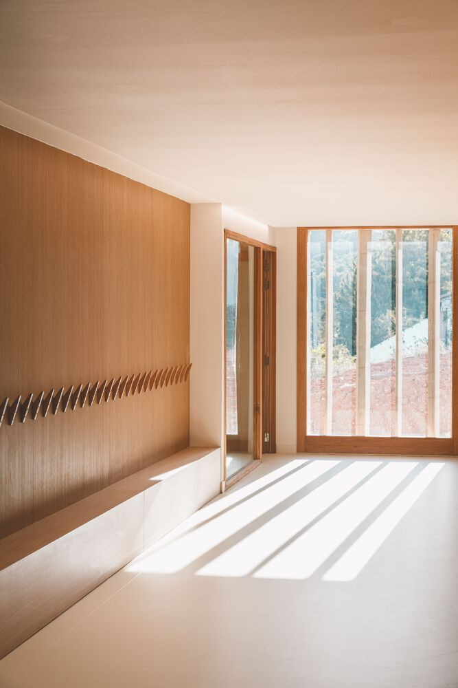 Interior space with oak wall and timber-framed glazing casting striped shadows across white resin floor