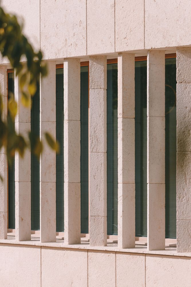 Facade detail with vertical green louvered vents set between stone panels in sunlight