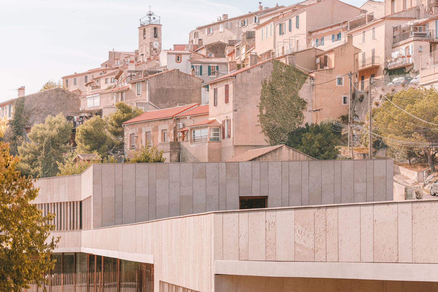 Stone-clad volumes nestled below a hillside village of terracotta-roofed buildings