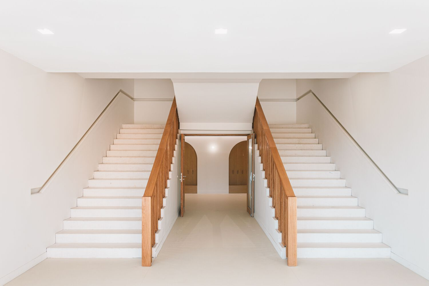 Symmetrical pair of staircases with timber balustrades converging on a central corridor below
