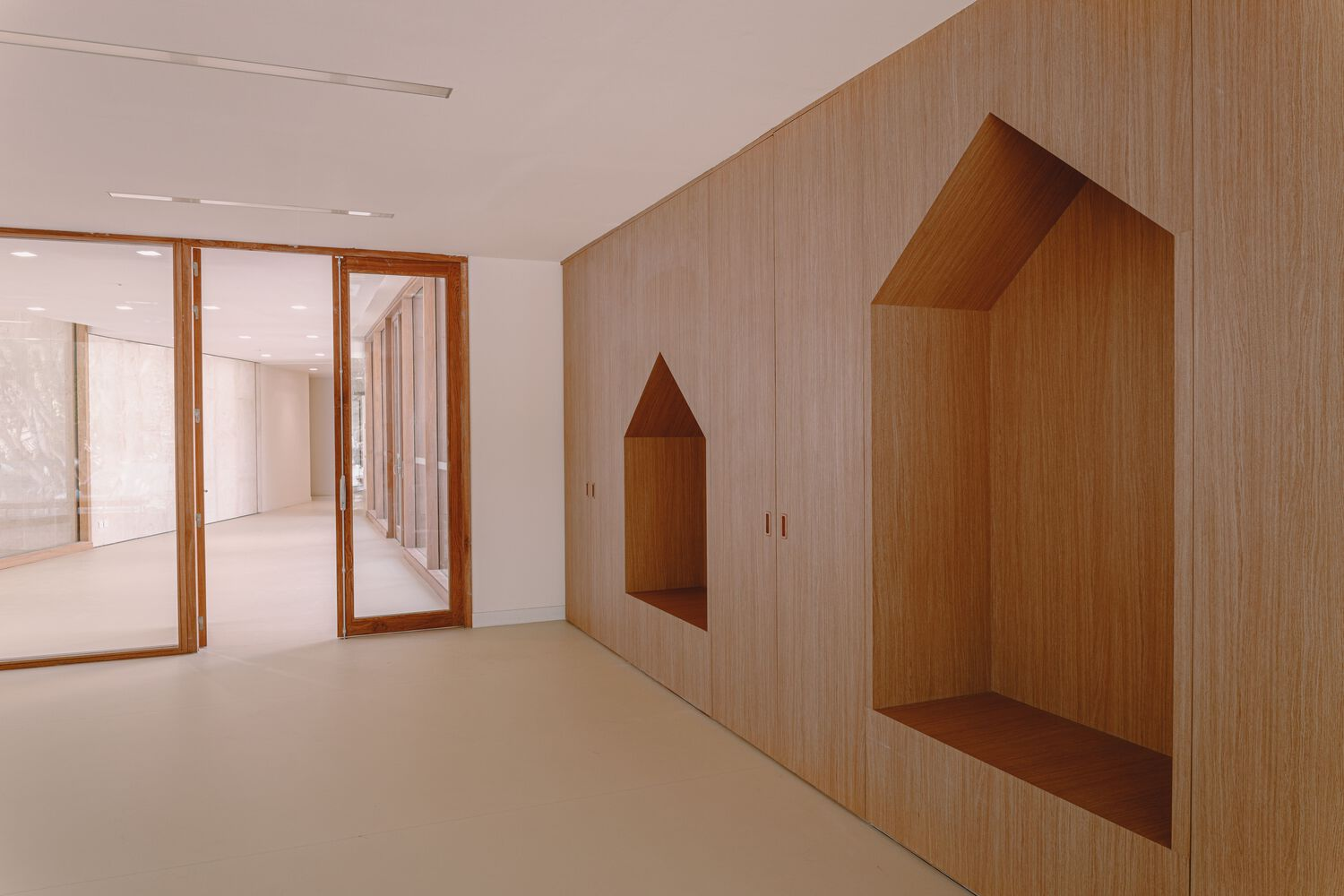 Interior wall with light wood paneling featuring house-shaped recessed niches beside timber-framed glass doors