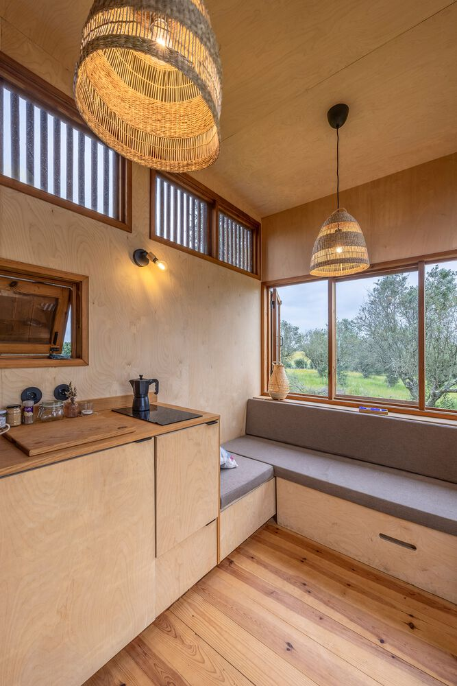 Compact kitchen with woven pendant lamps and window seat framed by timber details in daylight