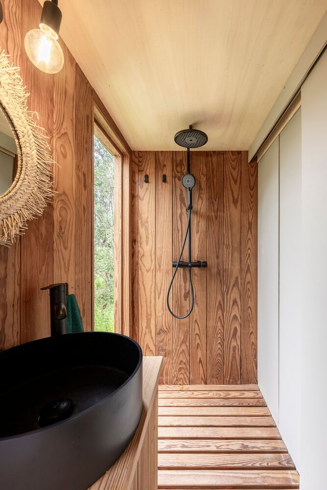 Bathroom with slatted timber floor, wall-mounted shower, circular sink and narrow vertical window overlooking trees