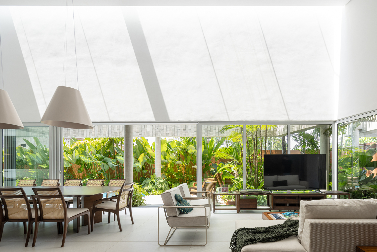 Open living and dining space with sloped skylight casting linear shadows above floor-to-ceiling garden windows