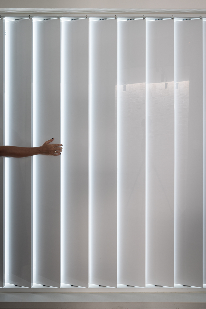 Vertical louver blinds with hand pulling one panel to adjust interior daylight