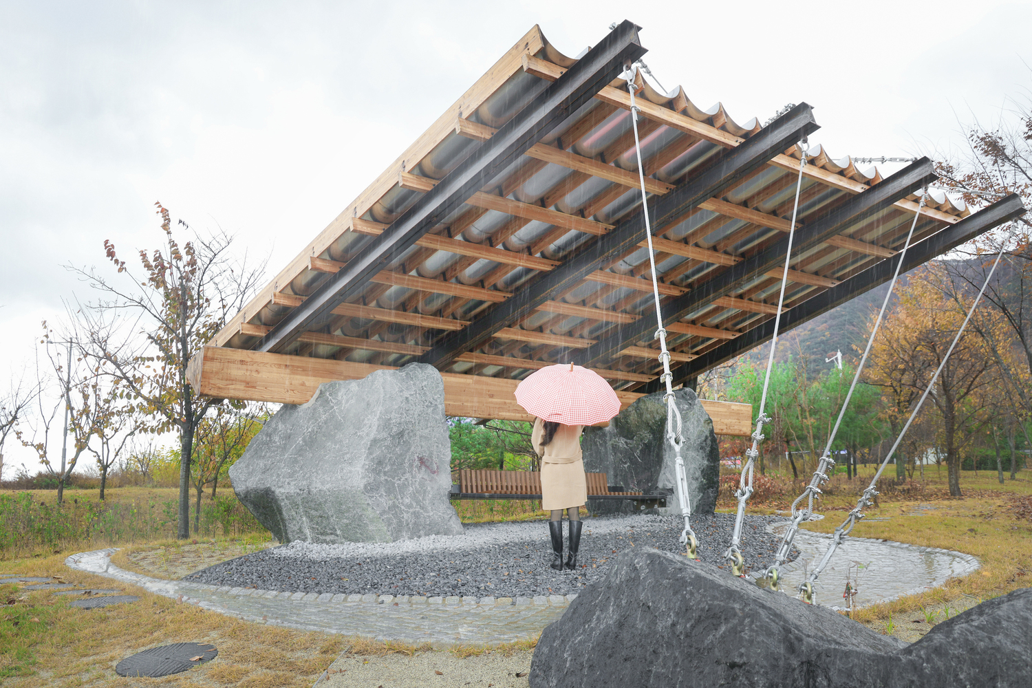 Exposed timber roof structure with cable suspension and a visitor holding a pink umbrella beneath